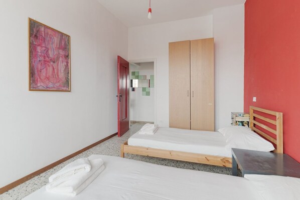 A room with two beds, a wooden wardrobe, a red wall, and a painting.