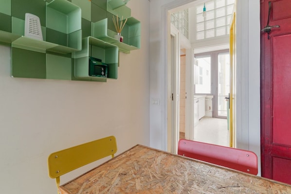 Una habitación con una cama de madera, contenedores de almacenamiento verdes, una puerta roja y vistas a través de un ventanal abierto.