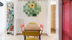 A dining area with a wooden table, chairs, and a green wall decoration. - GuestHost - Farini Apartment for 6 people Milan (Milan)