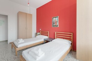 Une chambre avec deux lits simples, une armoire en bois, une petite table et une affiche accrochée au mur.