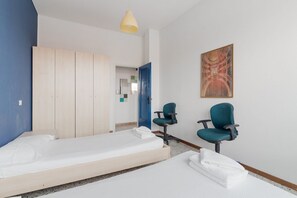 Ein Hotelzimmer mit zwei Betten, einer blauen Wand, einem Holzschrank, einem Schreibtisch mit Stuhl und einem Wandbild.