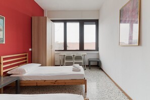 A room with two beds, a desk, chairs, a window, and a painting on the wall.