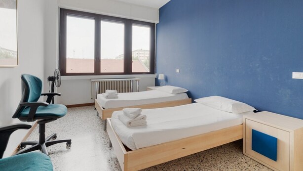 A bedroom with two beds, a chair, a desk, and a window. - GuestHost - Farini Apartment for 6 people Milan (Milan)