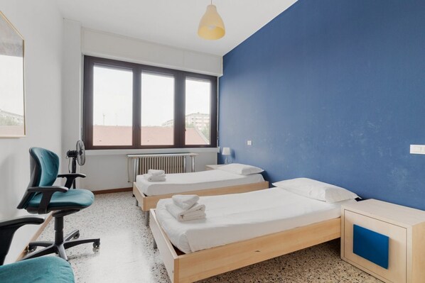 A bedroom with two beds, a chair, a desk, and a window.