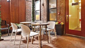 An outdoor patio area with brick flooring, wooden fence, and a brick wall. There are round tables and white perforated chairs. - Kasa the Duffy Times Square (New York)