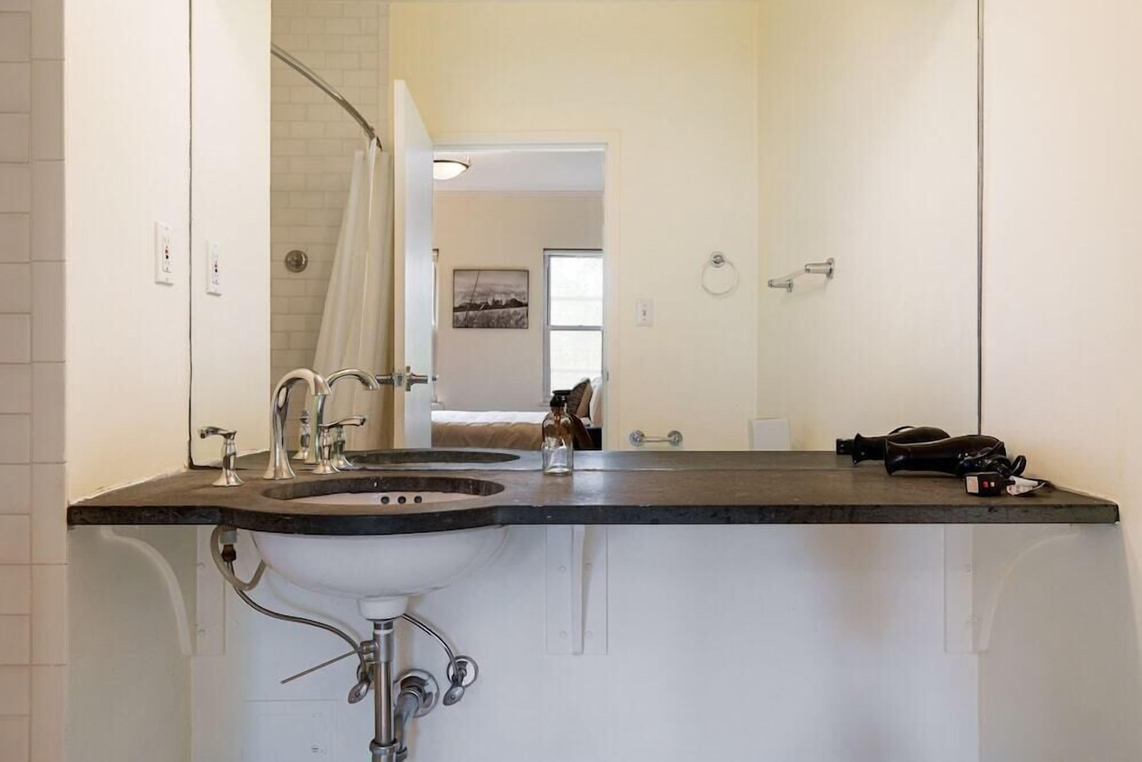 Une salle de bain avec un lavabo blanc, deux robinets, un miroir et un rideau de douche.