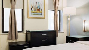 A hotel room with a bed, a dresser, a desk, and a lamp. There are curtains on the windows and a painting on the wall. - Kasa the Duffy Times Square (New York)