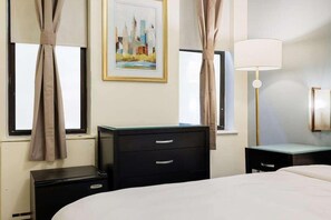 A hotel room with a bed, a dresser, a desk, and a lamp. There are curtains on the windows and a painting on the wall. - Kasa the Duffy Times Square (New York)