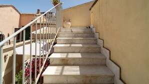 Eine Treppe aus Marmor führt zu einem Balkon mit Geländer, Kübelpflanzen und Blick auf angrenzende Gebäude.