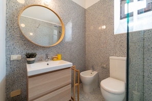 Une salle de bain moderne avec un lavabo sur pied, un miroir rond, un bidet et des toilettes.