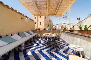 Une terrasse sur le toit avec un sol à motifs, un espace détente avec des coussins, une table avec des chaises et des plantes en pot.