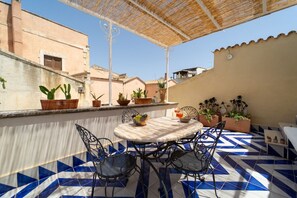 Une terrasse extérieure avec une table ronde et des chaises, des plantes en pot et un sol carrelé.