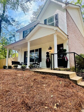A two-story house with a covered porch, a swing set, and a mailbox.