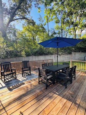 A wooden deck with a table and chairs, surrounded by a wooden fence and trees.