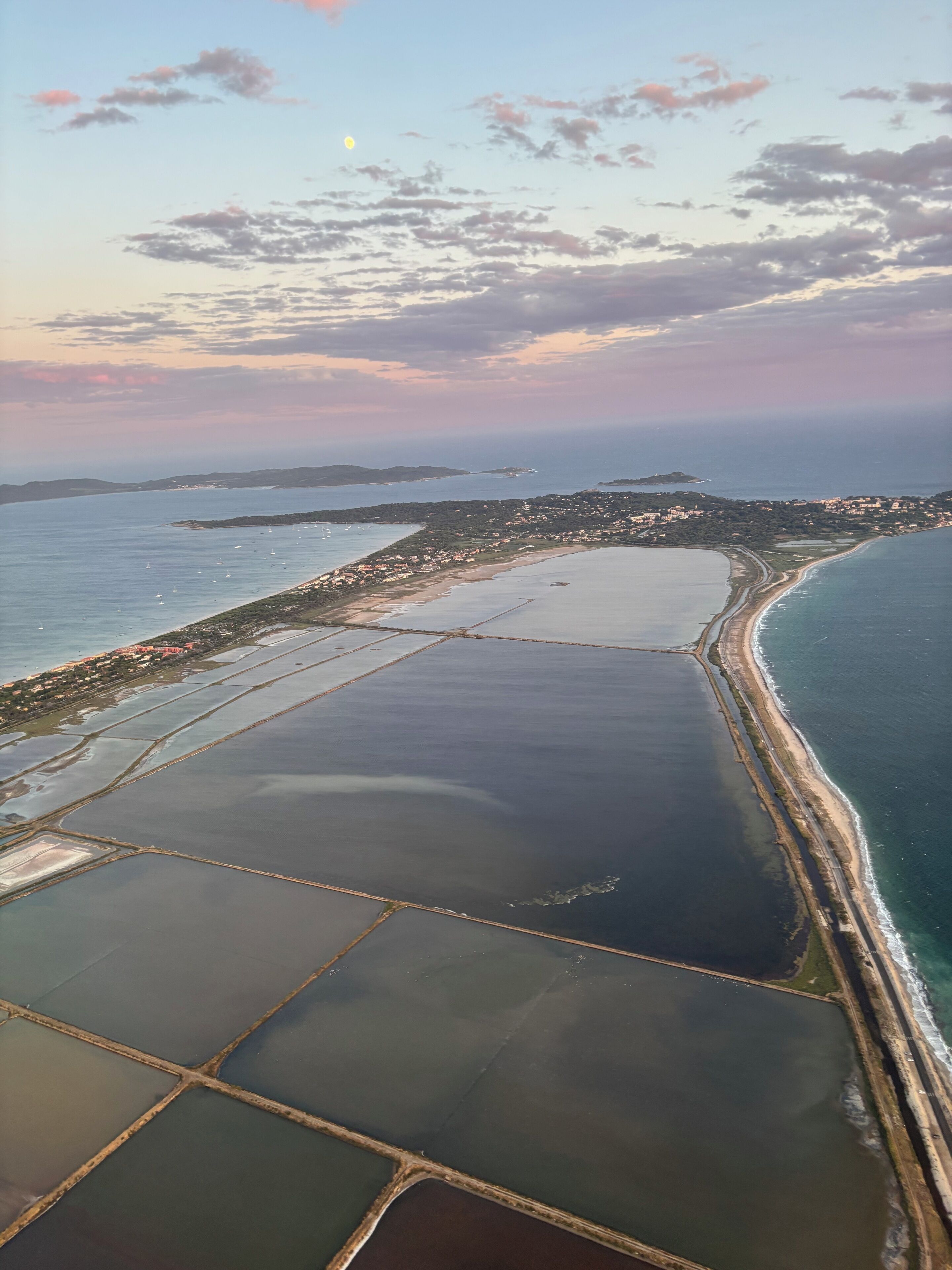 Ett flygbildsbild av ett kustområde med saltbassänger, en strand och en stad i bakgrunden.