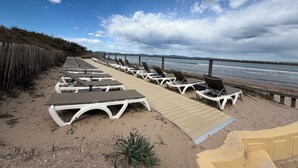 A beachside lounge area with sun loungers and a wooden walkway leading to the water. - Appt 2p-climatisé-WIFI-Parking-Pied dans l'eau-Plage La Badine-Presqu'ile Hyères (Hyères)