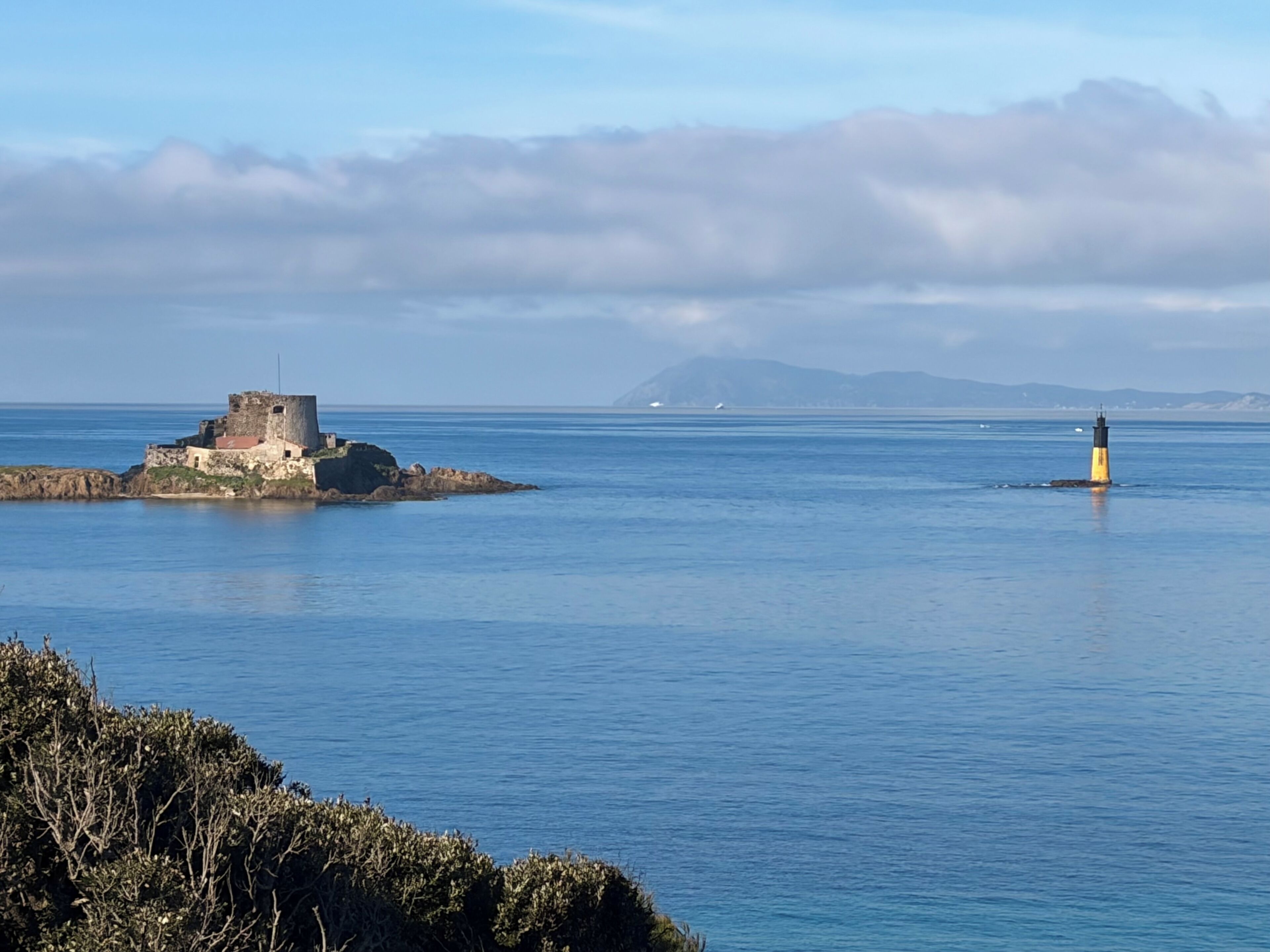 Paesaggio costiero con un faro e un edificio storico in pietra su una piccola isola.