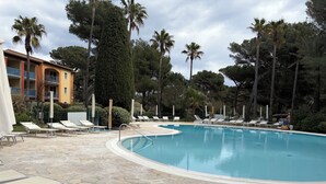 A swimming pool with lounge chairs and palm trees. - Appt 2p-climatisé-WIFI-Parking-Pied dans l'eau-Plage La Badine-Presqu'ile Hyères (Hyères)