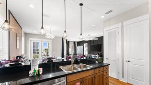 A modern kitchen with a black countertop, stainless steel sink, wooden cabinets, and pendant lighting.