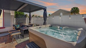 A hot tub area with a covered seating area, a patio with a patterned wall, and a sunset sky.