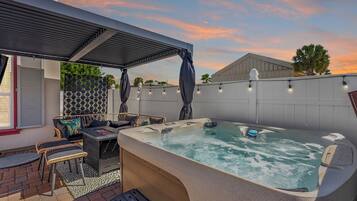 A hot tub area with a covered seating area, a patio with a patterned wall, and a sunset sky.
