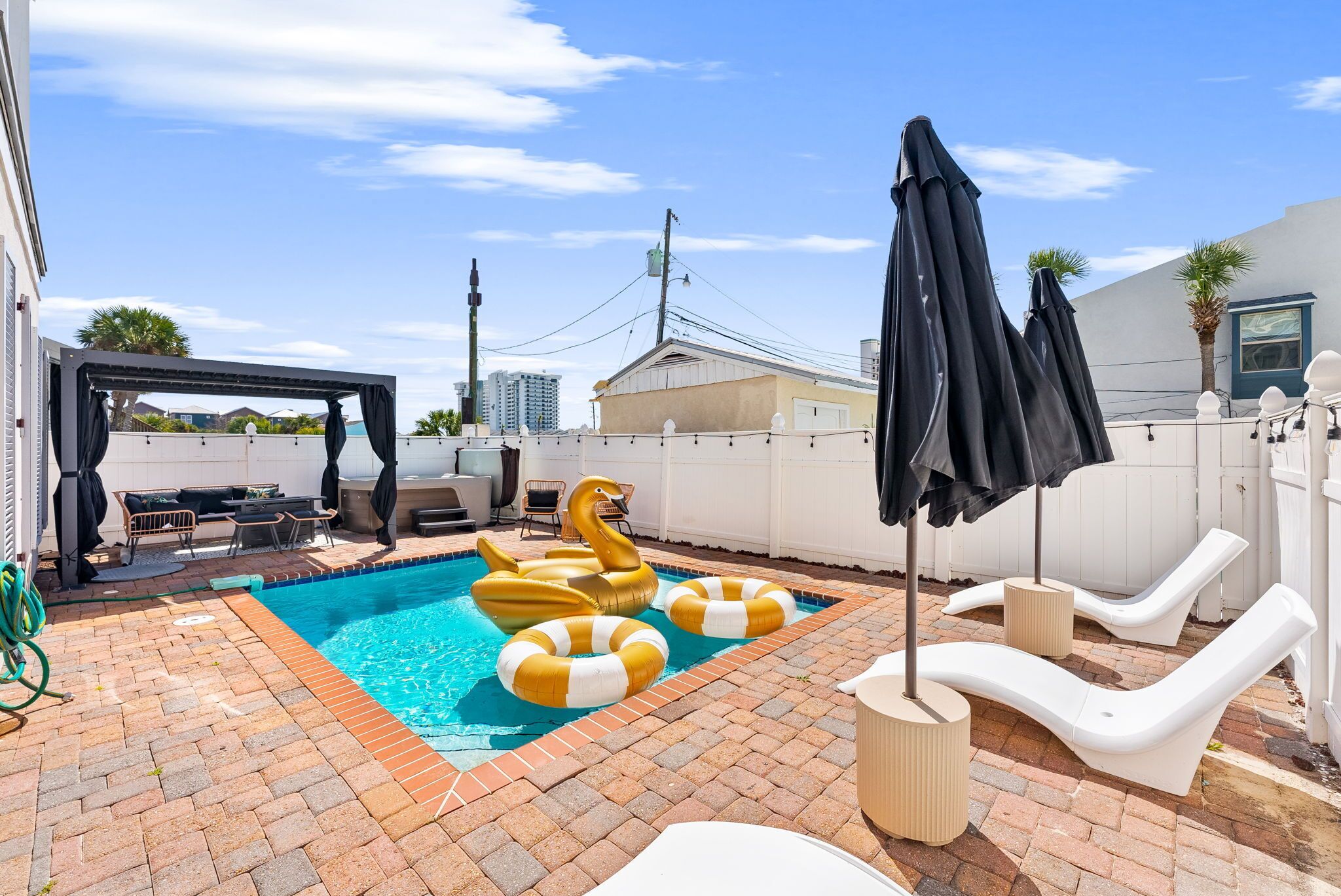 A backyard with a swimming pool, inflatable swan and ring floaties, lounge chairs, and a covered patio area.