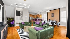 A modern living room with green sofas, a dining area, and a kitchen.