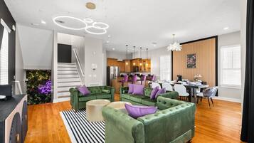 A modern living room with green sofas, a dining area, and a kitchen.
