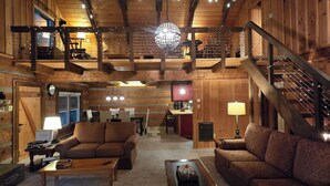A spacious log cabin interior with a high ceiling, wooden beams, a central chandelier, and a cozy seating area with sofas and a coffee table. - Peaceful Mountain Cabin over 4,600 ft elevation (Zionville)