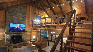 A spacious living area with a stone fireplace, a television, and a wooden staircase. - Peaceful Mountain Cabin over 4,600 ft elevation (Zionville)
