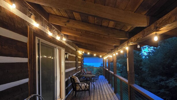 A wooden deck with string lights, a table, and chairs. - Peaceful Mountain Cabin over 4,600 ft elevation (Zionville)