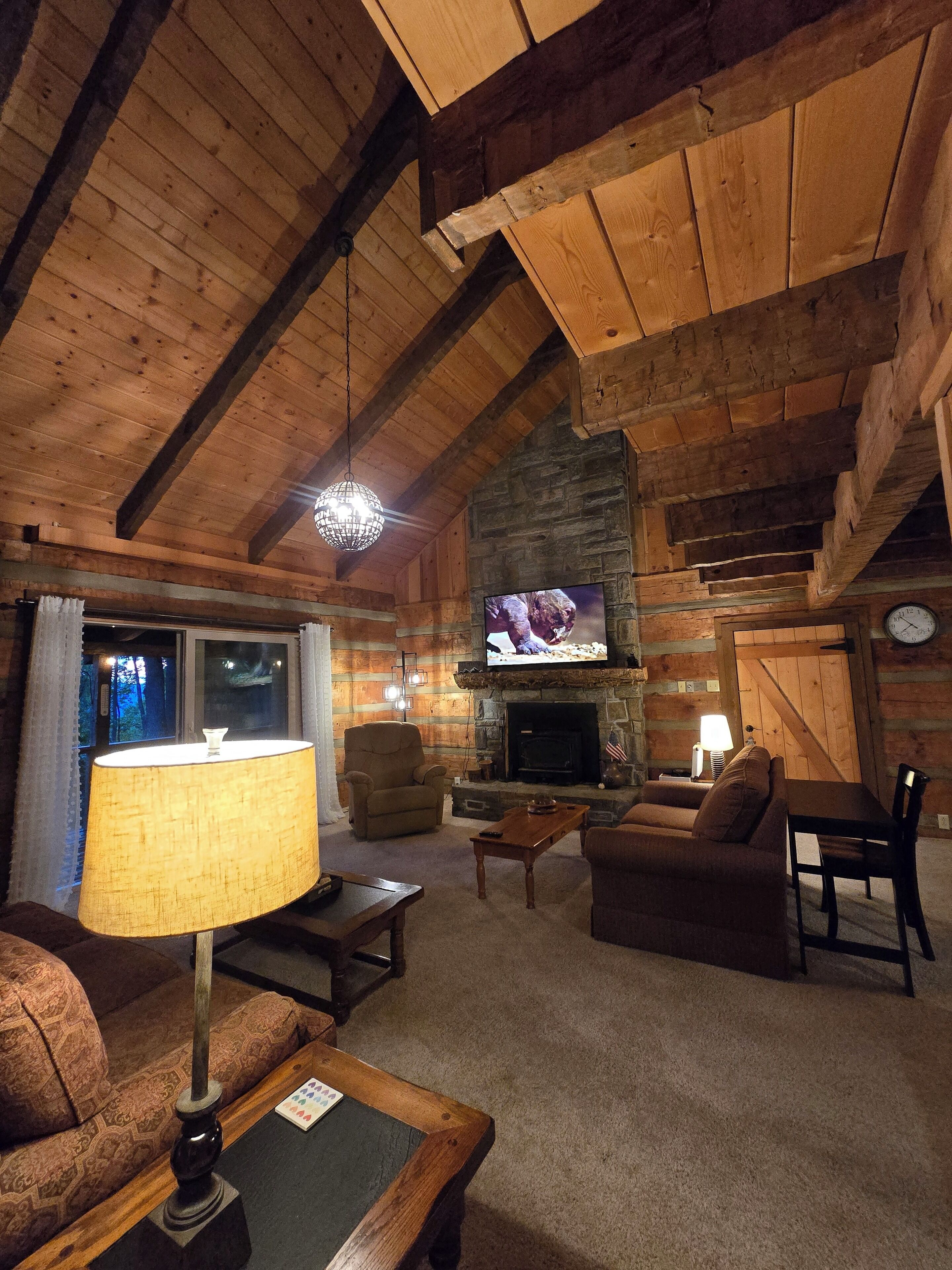 A cozy log cabin interior with a fireplace, wooden ceiling beams, a television, and comfortable seating.