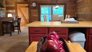 A wooden cabin interior with a dining area, a wooden table with a basket of red apples, a wooden bench, and a window with a view of trees. - Peaceful Mountain Cabin over 4,600 ft elevation (Zionville)