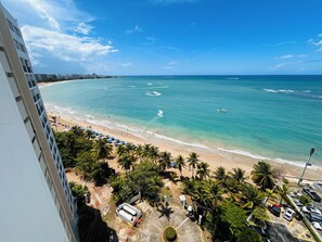 Un hôtel de grande hauteur surplombant une plage aux eaux turquoise et limpides, bordée de palmiers, et doté d’un parking.