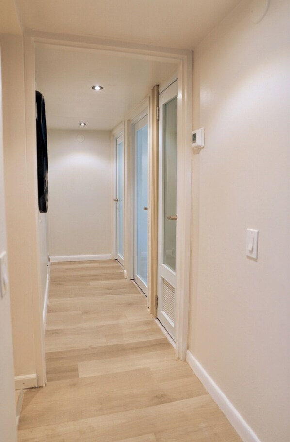 Un couloir doté d’un plancher en bois, de murs blancs et de portes avec des panneaux de verre.