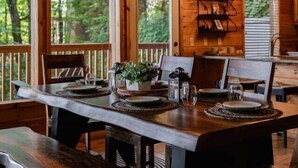 A wooden cabin interior with a dining table, benches, a chandelier, and a view of the forest. - Legends Lookout! Mtn Views, Bear sightings & More (Gatlinburg)