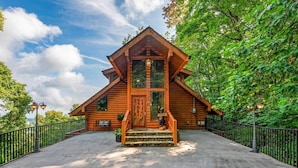 A wooden cabin with a steeply pitched roof, a front porch with steps, and a welcome sign. - Legends Lookout! Mtn Views, Bear sightings & More (Gatlinburg)