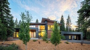 Ein modernes, zweistöckiges Haus mit großen Fenstern, einer Garage und einem gepflegten Garten mit Bäumen und Mulch.
