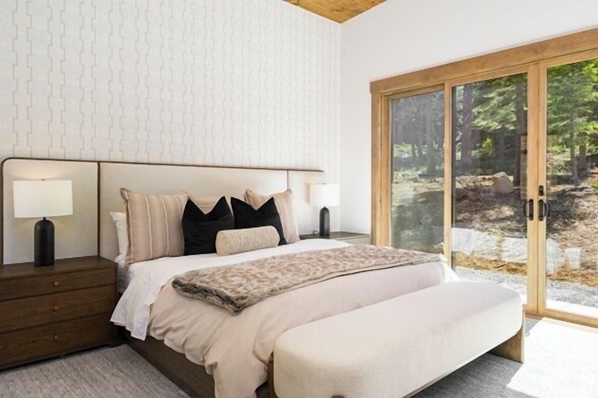 Un dormitorio moderno con una cama grande, una mesita de noche y vistas a un bosque a través de puertas de cristal.