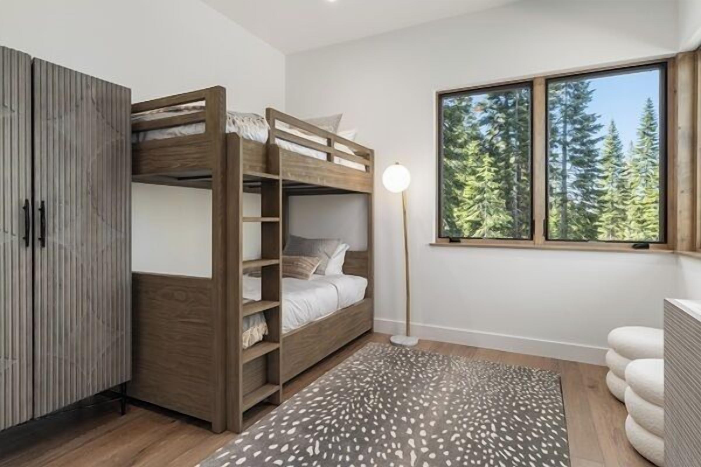 Habitación con literas, un armario, una lámpara de noche y una ventana con vistas al bosque.