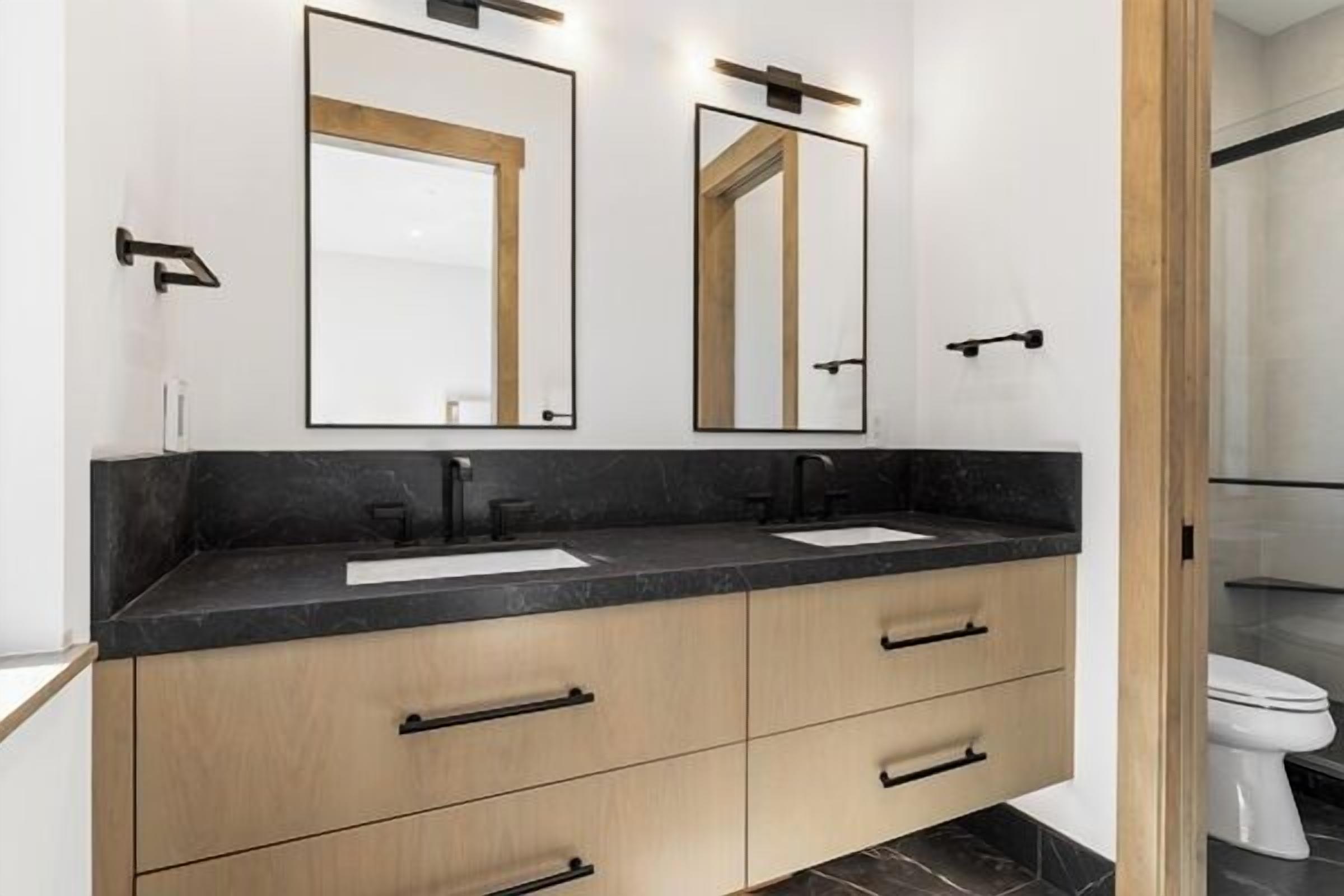 A modern bathroom with two sinks, wooden cabinets, and a large mirror.