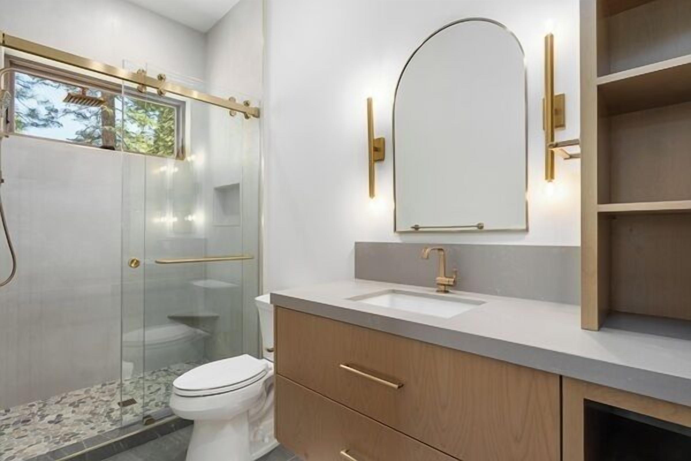 A modern bathroom with a glass shower enclosure, a white toilet, a wooden vanity with a sink, and a large mirror.