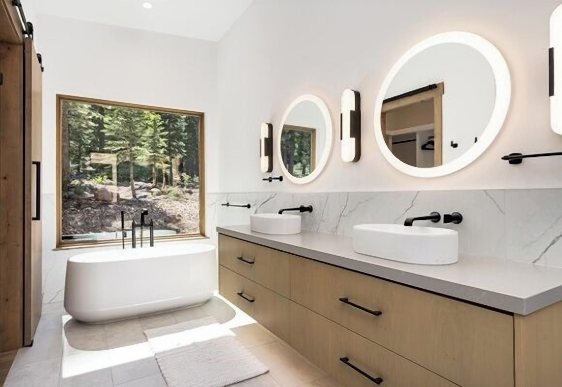 A modern bathroom with a freestanding bathtub, two sinks, and three wall-mounted mirrors.