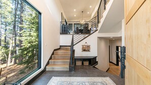 Um interior moderno com escada de madeira, uma grande janela com vista para uma floresta e uma placa de boas-vindas.