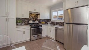 Una cocina moderna con armarios blancos, un refrigerador de acero inoxidable, horno empotrado y salpicadero de azulejos.