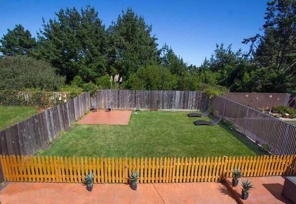 A fenced backyard with a grassy lawn, a patio area, and a wooden fence.