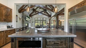 Una cocina amplia con una isla grande, vigas de madera, chimenea de piedra y electrodomésticos modernos.