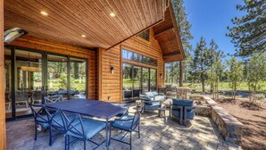 Una cabaña de troncos moderna con un patio que incluye una mesa y sillas para comer, una parrilla y una chimenea de piedra.