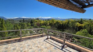 Un balcón con suelo de baldosas de piedra y barandilla de metal, con vistas a un paisaje montañoso de picos nevados y vegetación densa.