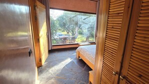 A bedroom with a large window, a bed, and a view of an outdoor dining area.